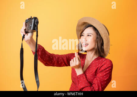 Gerne hübsche Frau eine selfie nehmen Sie ein Bild von der Kamera auf orangem Hintergrund, Asiatische Schönheit Stockfoto