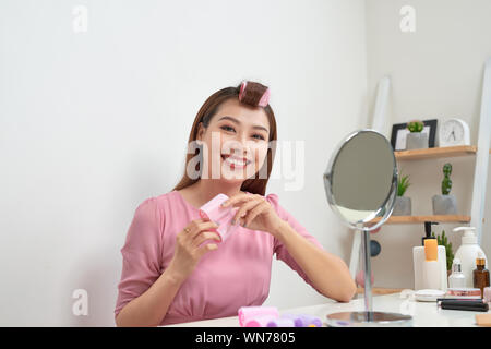 Kopf und Schultern Portrait von schöne asiatische Frau Haar Lockenwickler in Spiegel mit breitem Lächeln suchen, Home Interior auf Hintergrund Stockfoto