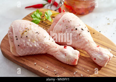 Zwei Rohmaterial Chicken Drumsticks mit Ihrer Haut bestreut mit Chili Flocken und Gewürze auf einem hölzernen Schneidebrett angezeigt in der Nähe zu sehen, geeignet für Stockfoto