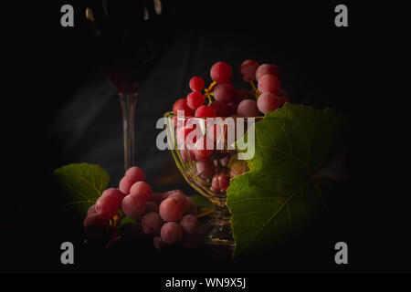 Trauben in die Schale. Grünen Weinblättern. Schwarzen Hintergrund. Zeit für Rotwein. Immer noch leben. Ein Glas Rotwein. Stockfoto