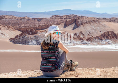 Junge blonde kaukasische Frau alleine sitzen und genießen Sie die unberührte Natur der Moon Valley in der Atacama-wüste, Chile. Herausragende Landschaft Hintergrund mit Stockfoto