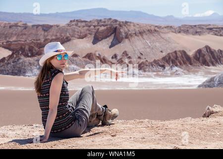 Junge blonde kaukasische Frau alleine sitzen und genießen Sie die unberührte Natur der Moon Valley in der Atacama-wüste, Chile. Herausragende Landschaft Hintergrund mit Stockfoto