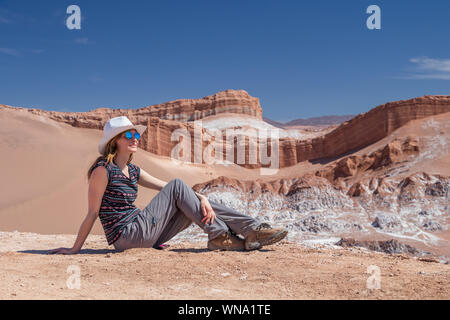 Junge blonde kaukasische Frau alleine sitzen und genießen Sie die unberührte Natur der Moon Valley in der Atacama-wüste, Chile. Herausragende Landschaft Hintergrund mit Stockfoto