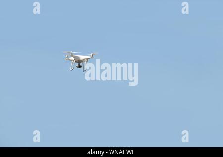 Big White drone schwebt in einem hellen wolkenlosen blauen Himmel, Radio Control Helicopter mit tragbaren Videokamera Versorgung Stockfoto