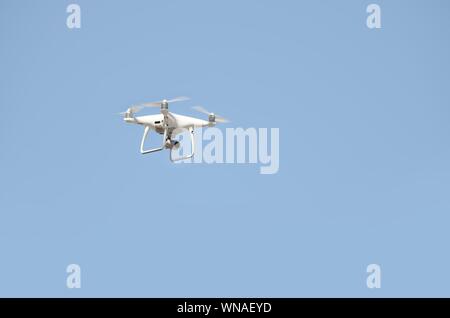 Big White drone schwebt in einem hellen wolkenlosen blauen Himmel, Radio Control Helicopter mit tragbaren Videokamera Versorgung Stockfoto