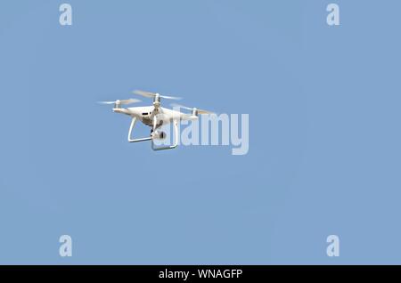 Big White drone schwebt in einem hellen wolkenlosen blauen Himmel, Radio Control Helicopter mit tragbaren Videokamera Versorgung Stockfoto