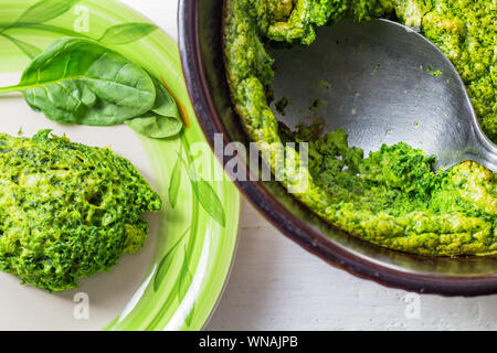 Gebackene Spinat souffle Souffle in Schale mit Löffel servieren und cremig flauschige Spinat auf Platte, Nahaufnahme, Ansicht von oben Foto Stockfoto