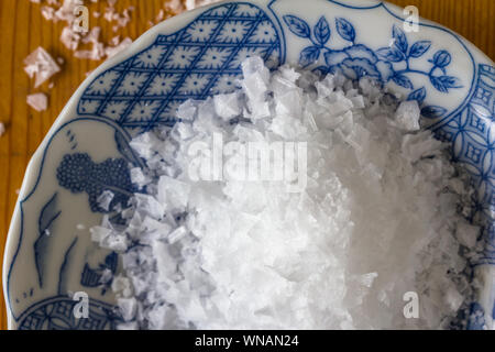 Zyprischen Salz Crystal Flakes in kleinen blauen und weißen Platte auf Holztisch - Ansicht von oben schließen Foto Stockfoto