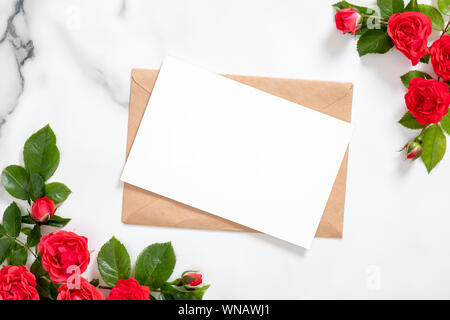 Leere Postkarte mit rosa Blüten Rahmen und craft-Umschlag auf Marmor Hintergrund. Grußkarte Mockup für Valentinstag, Mutter- oder der Frau Da Stockfoto