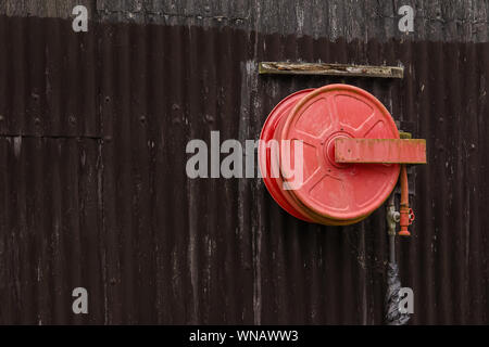 Roter Löschschlauch an der Seite eines schwarzen Wellblechgebäudes aufgewickelt Stockfoto