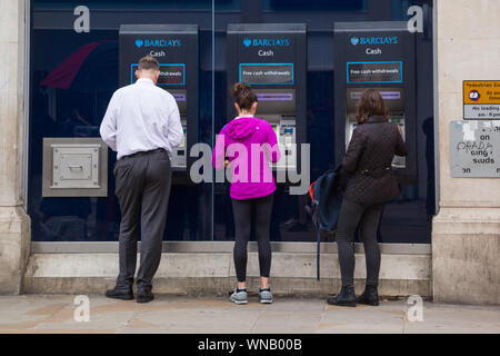Käufer nutzen drei Barclays Bank-Geldautomaten oder Geldautomaten außerhalb einer Filiale der Barclays Bank in der Hauptstraße. Stockfoto
