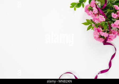 Bündel von rose Blumen in der rechten oberen Ecke und Purple ribbon auf weißem Hintergrund. Minimale flach Stil Komposition. Grußkarte mockup. Stockfoto
