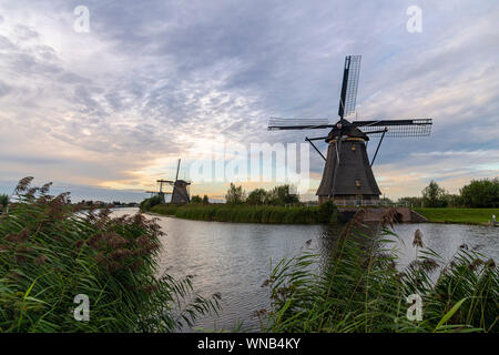 Holländische Windmühle auf dem ruhigen Kanalwasser in den frühen Sonnenuntergang leuchten wider Stockfoto
