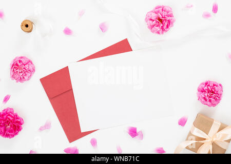 Minimale flach Stil Komposition mit einem roten Umschlag, weiße leere Karte und rosa Rosen Blumen auf weißem Hintergrund. Ansicht von oben Grußkarte mockup wit Stockfoto