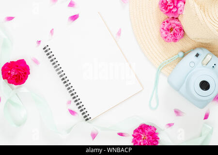 Ansicht von oben feminin Hintergrund mit Blumen und Elemente des Mädchens. Flach leeres Papier notepad, moderne instant Kamera, staw Hut, Ribbon, rosa Blumen o Stockfoto