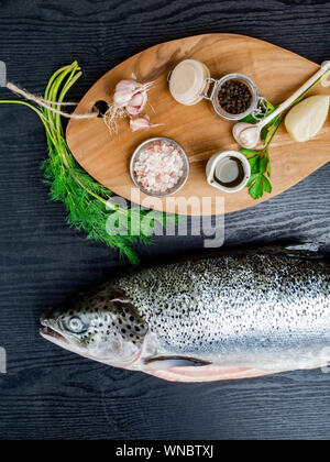 Frischen, rohen Lachs rot Fisch mit Gewürzen, Zitrone, Pfeffer, Kräutern auf dunklem Stein Hintergrund. Kreative Gestaltung aus Fisch, Ansicht von oben, flach Stockfoto