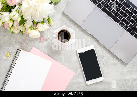 Stilvolle Betonstein Büro Schreibtisch Tisch mit Laptop, Tasse Kaffee, Blumen, weibliche Hand das Schreiben von Text in Papier Tagebuch Notepad. Ansicht von oben mit der Stockfoto