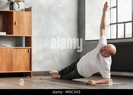Freundliche senior Hispanic Mann ein seitlicher Ganzkörperstütz Übung im Wohnzimmer. Yoga zu Hause im Alter. Stockfoto
