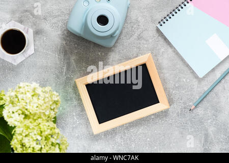 Ansicht von oben home office Schreibtisch mit femininen Zubehör und Geräte. Flach leeren Bilderrahmen, Papier notepad, Instant film Kamera, Kaffeetasse, Blumen Stockfoto