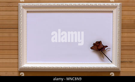 Weißer Rahmen mit einem getrocknete rote Rose und leeren weißen Leinwand auf natürlichem Bambus Wand. Horizontale Bild 16:9 mit nützlichen Design für Ihren Text. Stockfoto