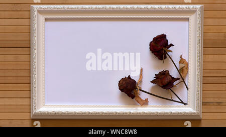 Weißer Rahmen mit drei getrocknete rote Rosen und weiße Leinwand auf natürliche Bambus Wand. Horizontale Bild 16:9 mit nützlichen Design für die Eingabe von Text in Stockfoto