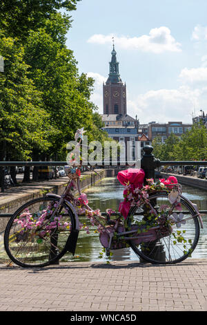 Rosa Fahrrad parken auf der Brücke über das ruhige Wasser von einem Kanal mit einem Schiff eine Rundreise zu den Touristen, Amsterdam, Niederlande Stockfoto