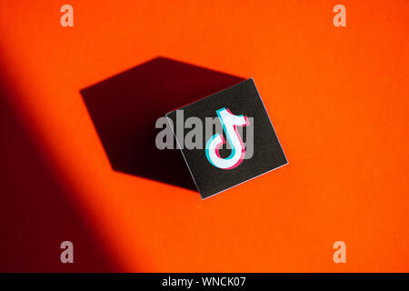 Ein Schuß von oben Papier Kubus mit den gedruckten Firmenlogo der TikTok Anwendung, die auf einem orangefarbenen Hintergrund platziert. Stockfoto