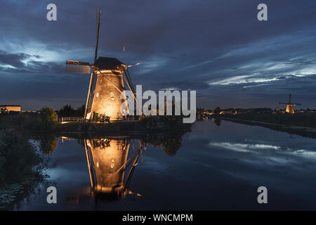 Beleuchtete Mühle spiegelt sich auf dem ruhigen Kanal Wasser während der bleu Stunde Sonnenuntergang in Alblasserdam, Niederlande Stockfoto