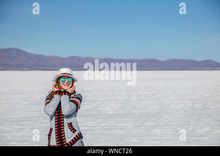 Junge Frau Porträt. Weibliche Person reisen Mädchen glücklich und lächelnd in weißen Salzsee Uyuni, Bolivien. Kaukasische Casual Model freudig trug Hut und Stockfoto