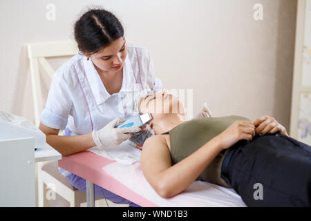 Kosmetikerin macht Ultraschall Peeling für weibliche Kunden. Kosmetiker dabei Verfahren der Reinigung mit Ultraschall Wäscher. Im Schönheitssalon. Stockfoto