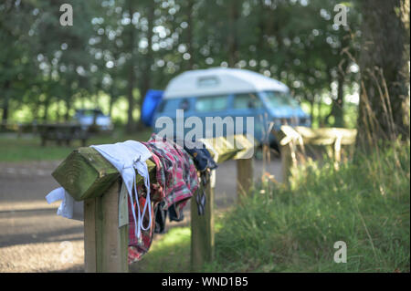 Sportliche Kleidung trocknen in der Sonne auf einem Campingplatz nach einer Wanderung bei Sonnenaufgang mit Wohnmobil und Sonnenstrahlen im Hintergrund Stockfoto