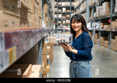 Junge asiatische Frau Prüfer oder Trainee Personal Arbeit suchen und prüft die Anzahl der Elemente speichern von digitalen Tablet. Asiatische Eigentümer oder Small Business conce Stockfoto