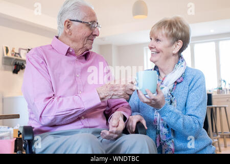 Ältere Frau Übergabe Mann im Rollstuhl heißen Getränk zu Hause Stockfoto