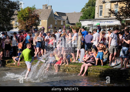 August Bank Holiday Festlichkeiten in Bourton-on-the Wasser Gloucestershire, Großbritannien. Die traditionelle Fußball in den Fluss. Spritzer in die Menge. Stockfoto