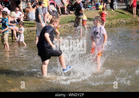 August Bank Holiday Festlichkeiten in Bourton-on-the Wasser Gloucestershire, Großbritannien. Paddeln in den Fluss. Stockfoto