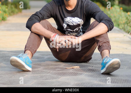 Close up 7/8 Image der jungen Sportler, Sportler Mann im Sport Kleidung sitzen auf der Schiene und im Feld in der Nähe von Spielplatz und entspannend nach dem Joggen oder Krieg Stockfoto