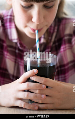 Mädchen Trinken von zuckerhaltigen Fizzy Soda aus Glas mit Strohhalm Stockfoto