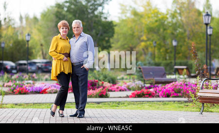 Mann und Frau von 60 Jahren stehen neben einander umarmen unter den Blumen Stockfoto