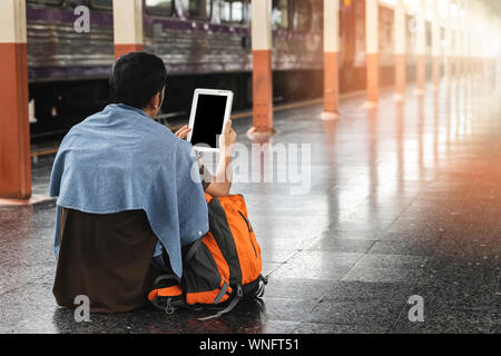 Ein Mann mit digitalen Tablet sitzen auf dem Boden am Bahnhof. Stockfoto