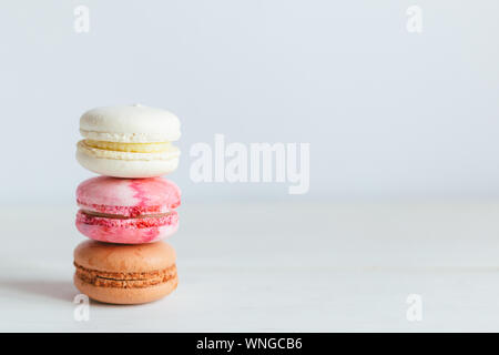 Drei französische Macarons auf einem weißen Holztisch. Bunte macarons. Weißer Hintergrund. Minimalkonzept, Platz für Text. Stockfoto