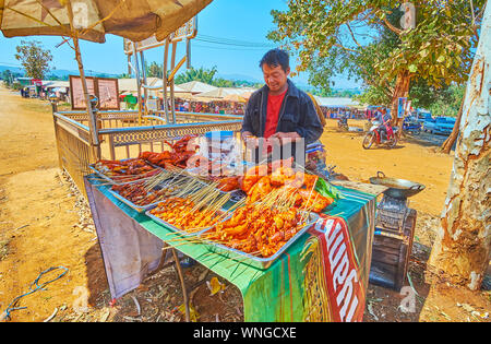 KAKKU, MYANMAR - Februar 20, 2018: Die Straße essen Anbieter gegrillte Hähnchen am Spieß bietet am Eingang Kakku Markt, am 20. Februar in Kakku. Stockfoto