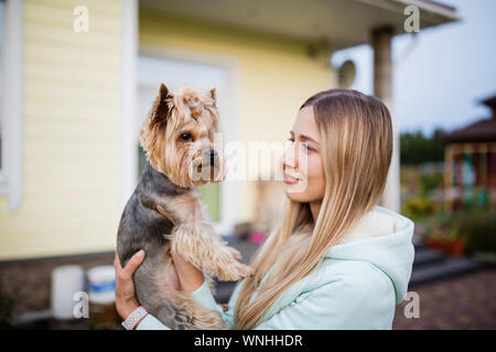 Hübsche Frau mit langen blonden Haaren kleiner Hund Yorkshire Terrier outdoor Holding Stockfoto