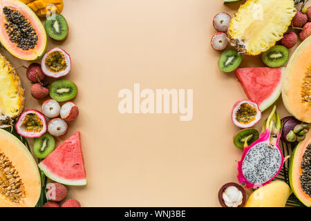 Frische exotische Früchte und tropischen Palmen Blätter auf pastellorange Hintergrund - Papaya, Mango, Ananas, Passionsfrucht, Dragon Obst, Trauben, lichee, Kiwi Stockfoto