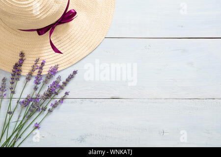 Flatlay feminine Schreibtisch mit Strohhut und Lavendelblüten auf rustikalen blau Holz- Hintergrund. Flach, Ansicht von oben, kopieren. Sommer Mode Konzept. Stockfoto