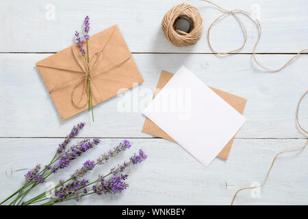 Feminine Arbeitsbereich mit Lavendelblüten, Handwerk Papier Umschlag, Garn, leeres Papier Karte mockup auf blauem Hintergrund. Romantische Brief, liebe Nachricht conce Stockfoto