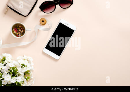 Flatlay Zusammensetzung mit femininen Zubehör, Tasse Tee, Smartphone leerer Bildschirm Mockup, Sonnenbrille, daisy flowers auf Pastell rosa Hintergrund. Weiblich Stockfoto