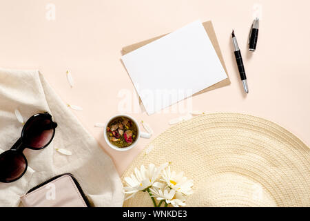 Flatlay Komposition mit Sommer Mode Accessoires, Strohhut, Kleidung, Tee Tasse, leeres Papier Karte Mockup, daisy flowers auf Pastell rosa Hintergrund. Fl Stockfoto