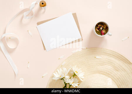 Flatlay Komposition mit leerem Papier Karte Mockup, Umschlag Strohhut, Daisy Blumen, Kaffee Tasse, Band auf Pastell rosa Hintergrund. Flach, Ansicht von oben, Co Stockfoto