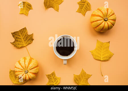 Herbst Rahmen aus Kürbissen, Tasse Kaffee und Laub auf orangem Hintergrund. Herbst, Halloween und Thanksgiving Konzept. Styled Lager flach Stockfoto