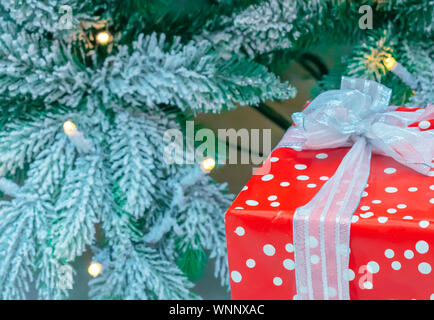 Ein Geschenk in roter Verpackung auf dem Hintergrund einer schneebedeckten Weihnachtsbaum. Stockfoto